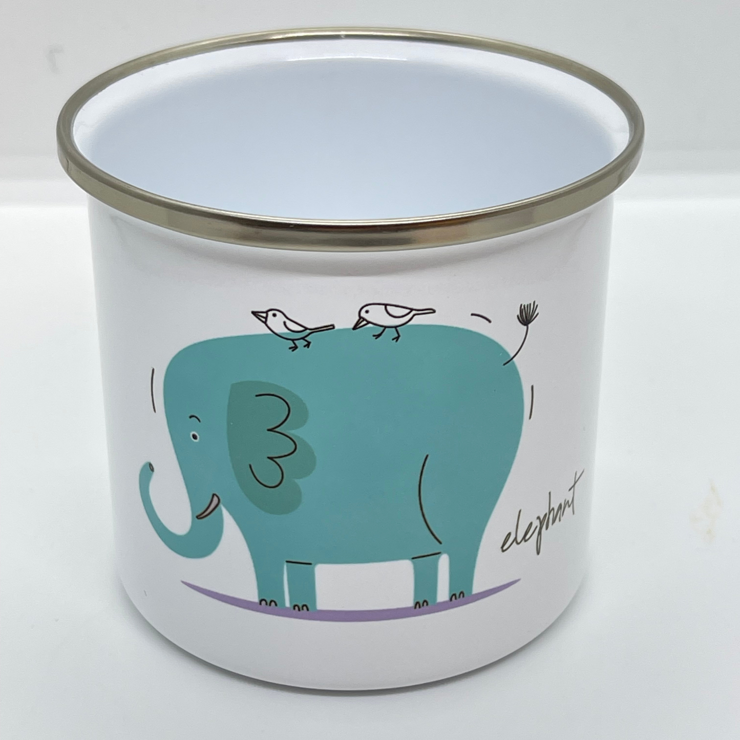 Emaljekrus i hvit farge med håndtak og en dekorativ sølvkant øverst. Kruset er påført et trykk med en grønn Elefant. Volum 32 cl. Diameter 8 cm.  Høyde 8 cm.