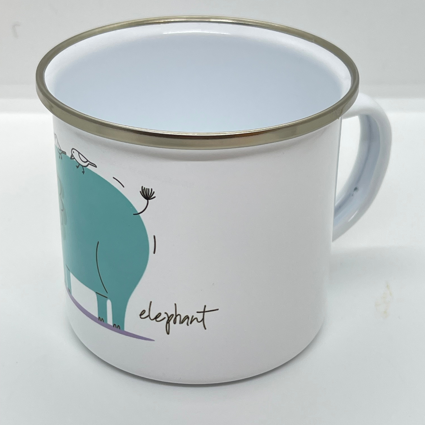 Emaljekrus i hvit farge med håndtak og en dekorativ sølvkant øverst. Kruset er påført et trykk med en grønn Elefant. Volum 32 cl. Diameter 8 cm.  Høyde 8 cm.