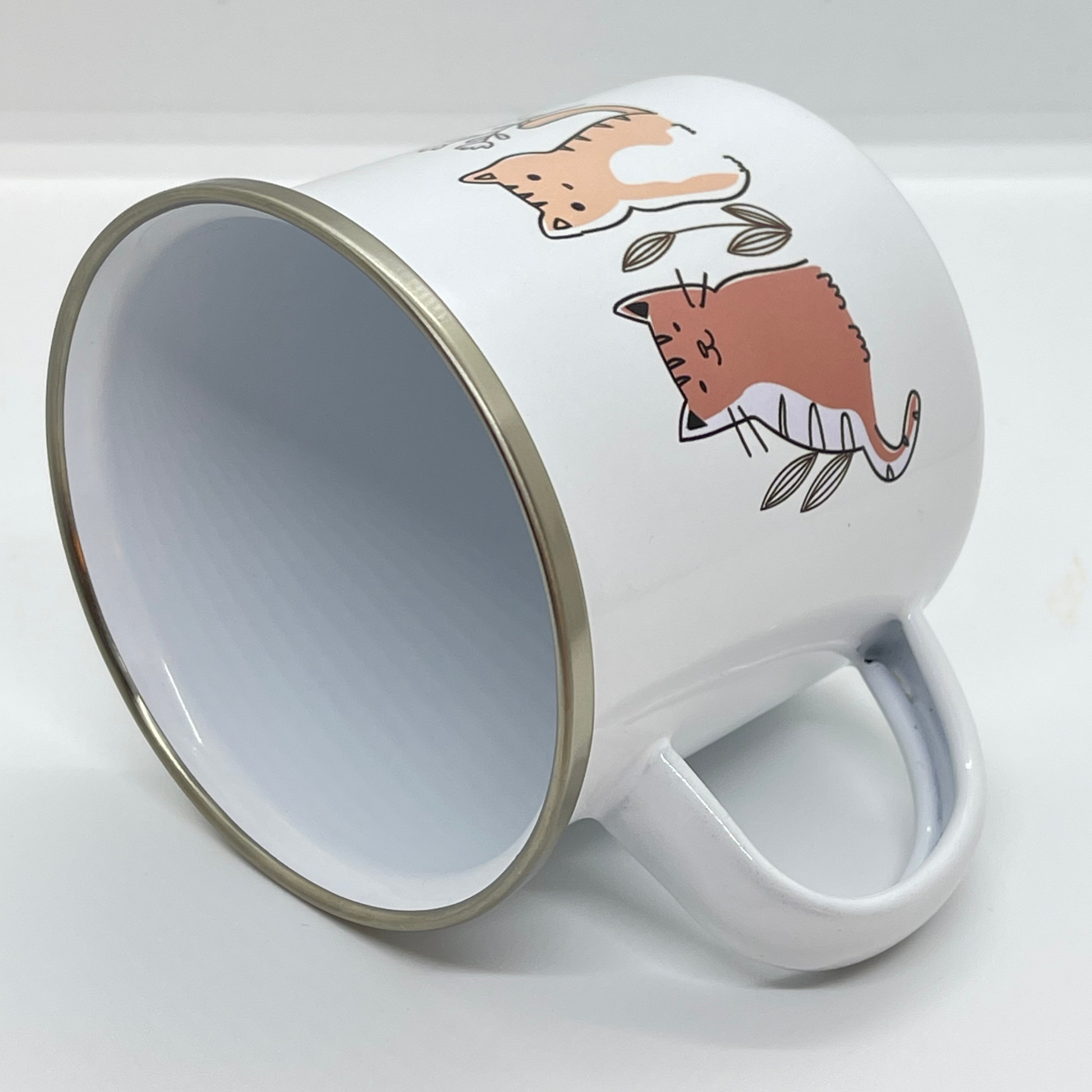Emaljekrus i hvit farge med håndtak og en dekorativ sølvkant øverst. Kruset er påført et trykk med Katter. Volum 32 cl. Diameter 8 cm.  Høyde 8 cm.