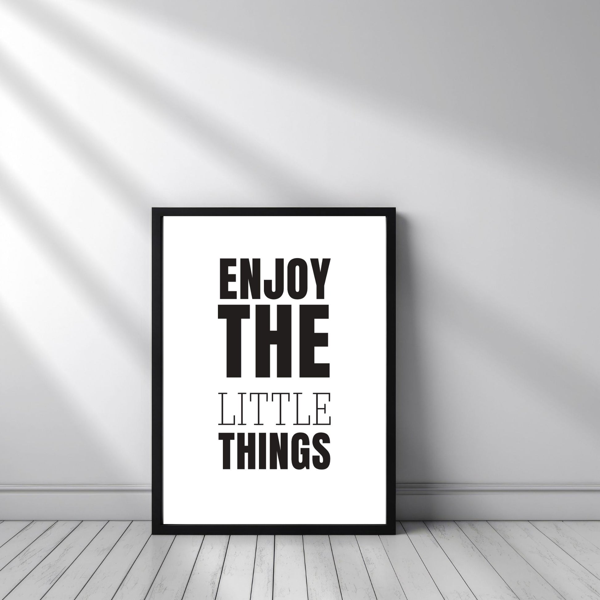Grafisk plakat med sort skrift på hvit bakgrunn. Tekst på plakat "Enjoy the little things" Illustrasjon viser plakat i sort ramme.