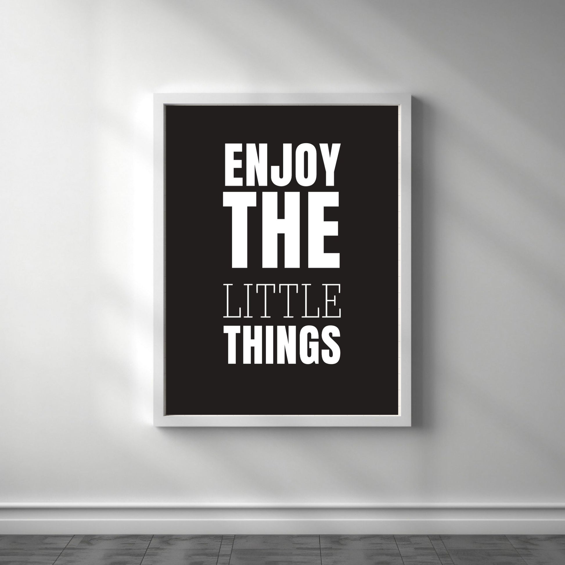 Grafisk plakat med hvit skrift på sort bakgrunn. Tekst på plakat "Enjoy the little things" Illustrasjon viser plakat i hvit ramme.