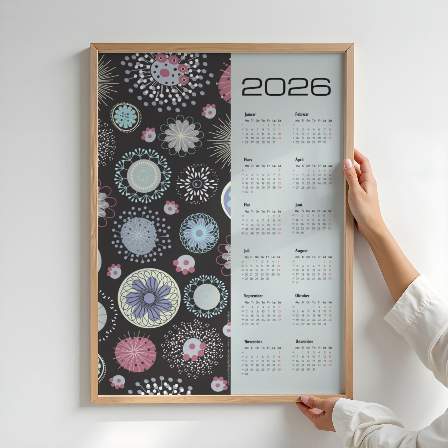 Grafisk kalender 2026 med pastellfargede abstrakte sirkler og mønstre på sort bakgrunn, med tydelig kalender og norske helligdager. Illustrasjon viser kalender i eik ramme.