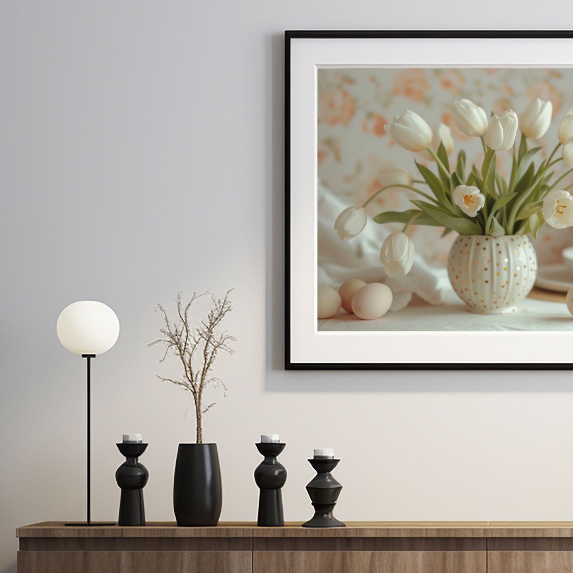 Grafisk illustrasjon av en rund, hvit vase med gullprikker, fylt med hvite tulipaner. Ved siden av vase ligger noen hvite påskeeg. Illustrasjonsbilde av plakat i sort ramme som henger på en vegg over en sjenk.