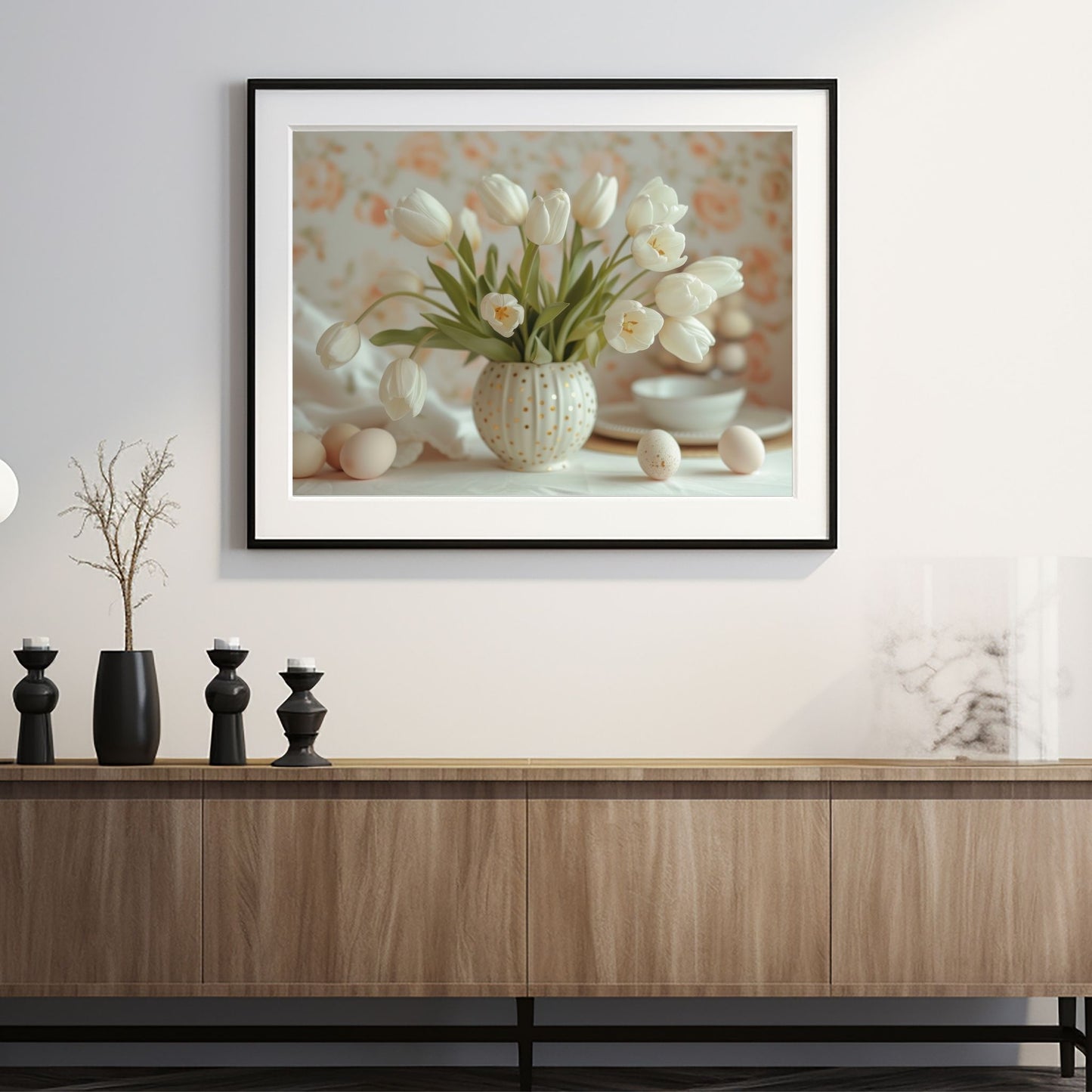 Grafisk illustrasjon av en rund, hvit vase med gullprikker, fylt med hvite tulipaner. Ved siden av vase ligger noen hvite påskeeg. Illustrasjonsbilde av plakat i sort ramme som henger på en vegg over en sjenk.