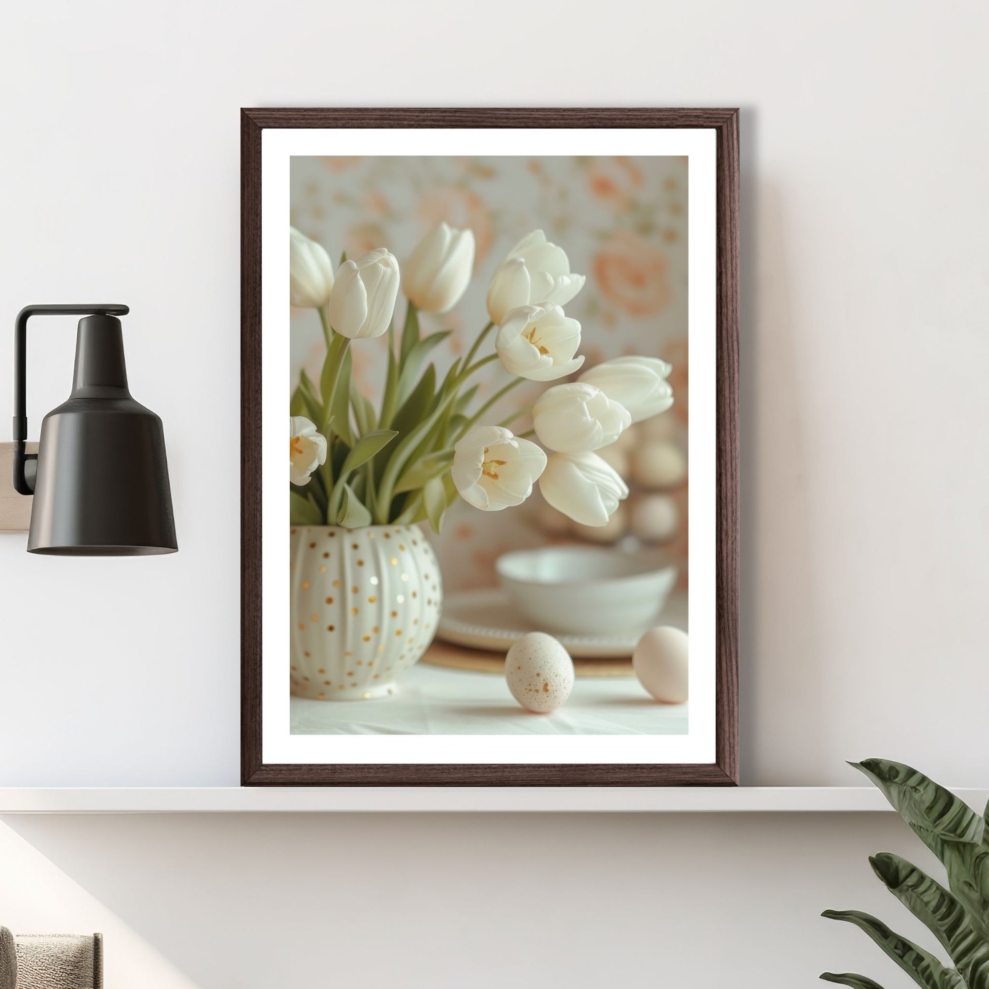 Grafisk illustrasjon av en rund, hvit vase med gullprikker, fylt med hvite tulipaner. Ved siden av vase ligger noen hvite påskeeg. Illustrasjonsbilde av plakat i brun ramme som står på en hylle.