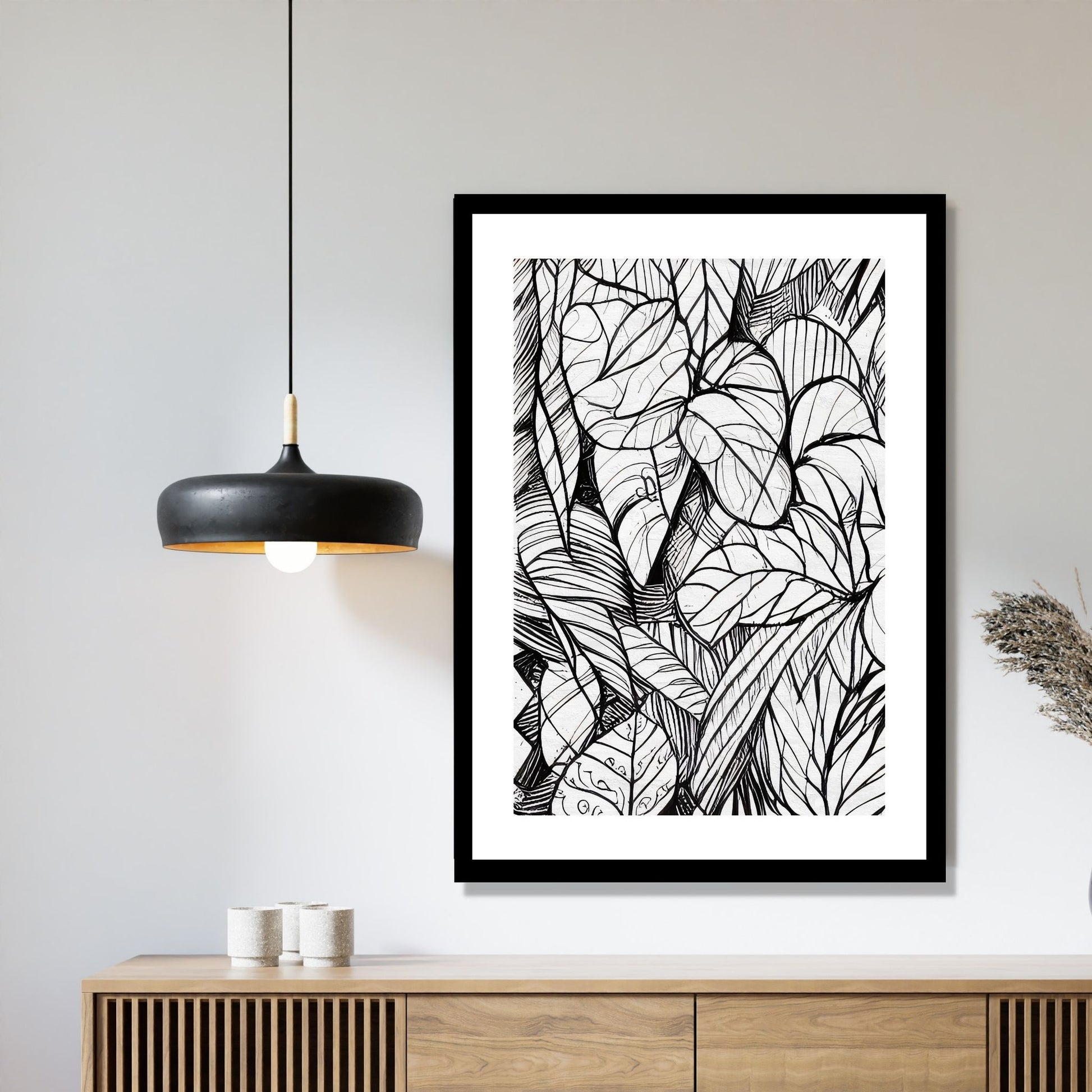Miljøbildet viser en grafisk plakat i abstrakt, floralt mønster i sort-hvitt. Plakaten som har en dekorativ hvit kant, henger i en sort ramme over en skjenk i teak. Ved siden henger en sort lampe.
