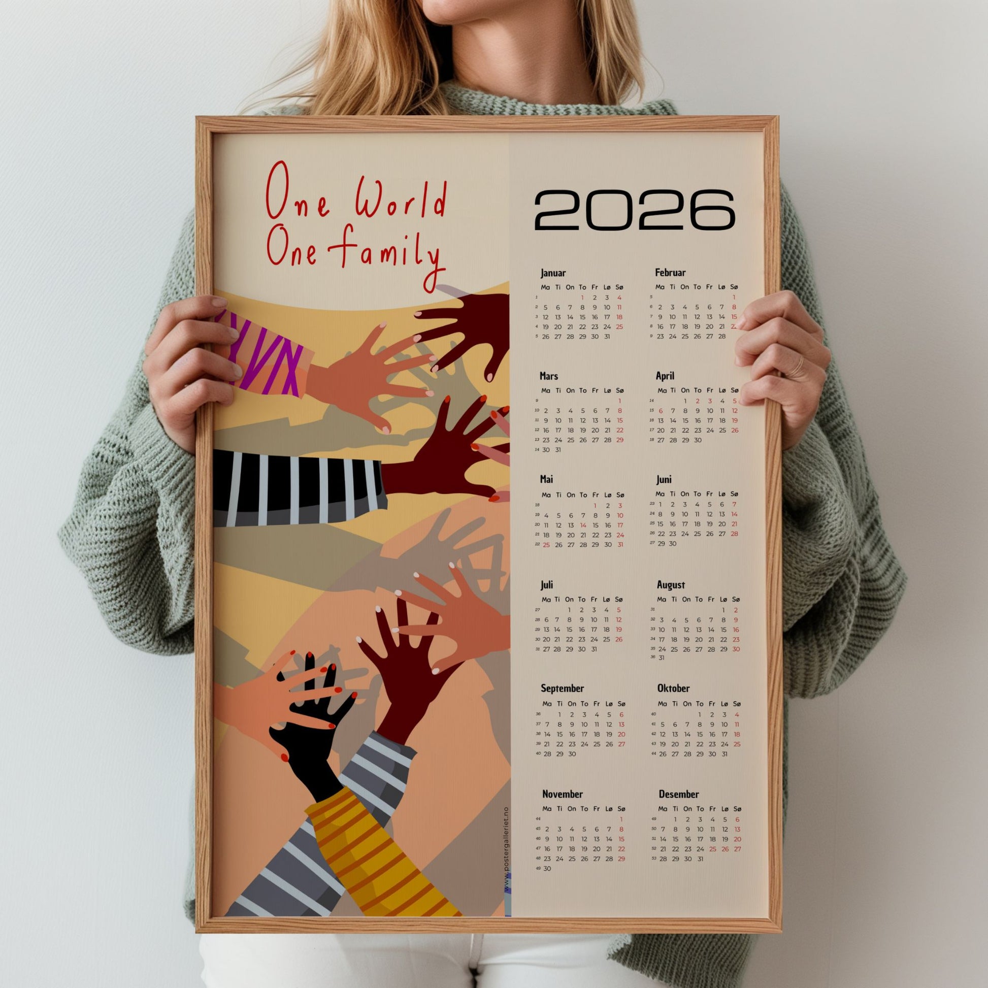 Kalender for 2026 med grafisk kunstmotiv av hender i ulike hudtoner og teksten One World – One Family. Kalenderen viser alle årets måneder på høyre side. Illustrasjon viser kalender i eik ramme.
