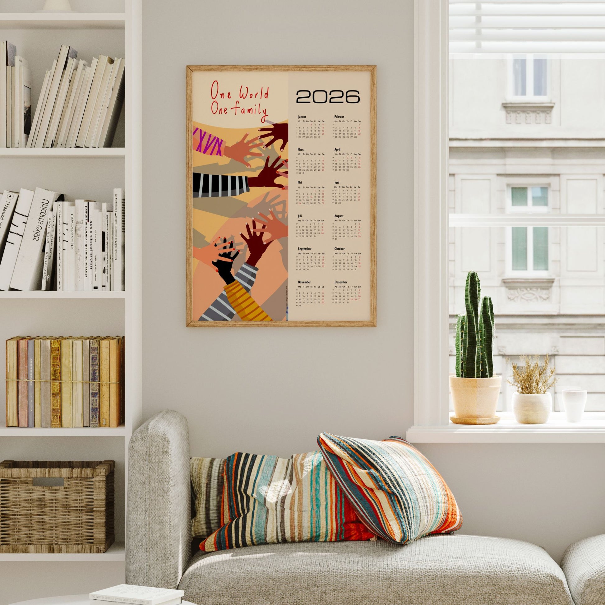 Kalender for 2026 med grafisk kunstmotiv av hender i ulike hudtoner og teksten One World – One Family. Kalenderen viser alle årets måneder på høyre side. Illustrasjon viser kalender i eik ramme.