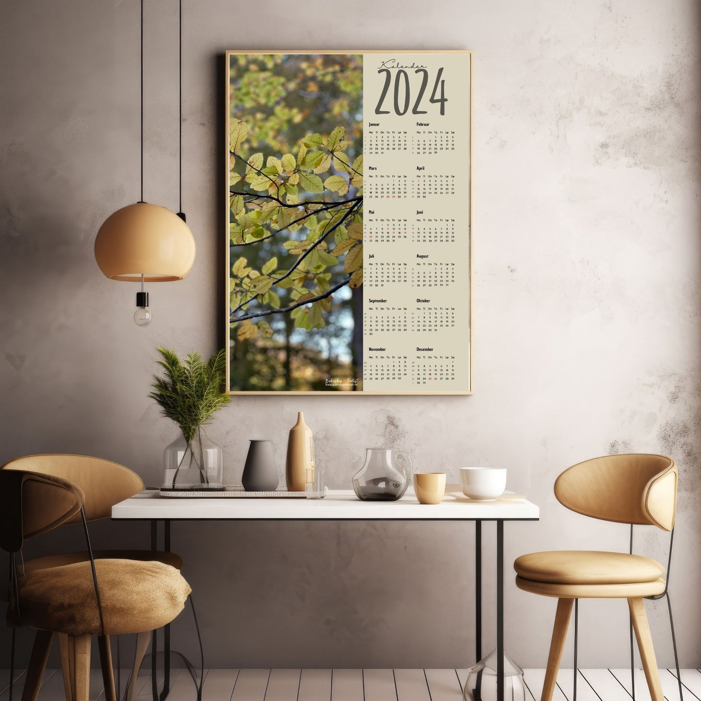 Kalender 2024 i grafisk print med fotomotiv. Halve vertikale side har et fotomotiv av en bøkeskog i høstfarger. Den andre halvdelen er påført 12 måneder med ukenummer og anmerket høytidsdager. Miljøbilde av kalender i eikeramme som henger på en vegg.