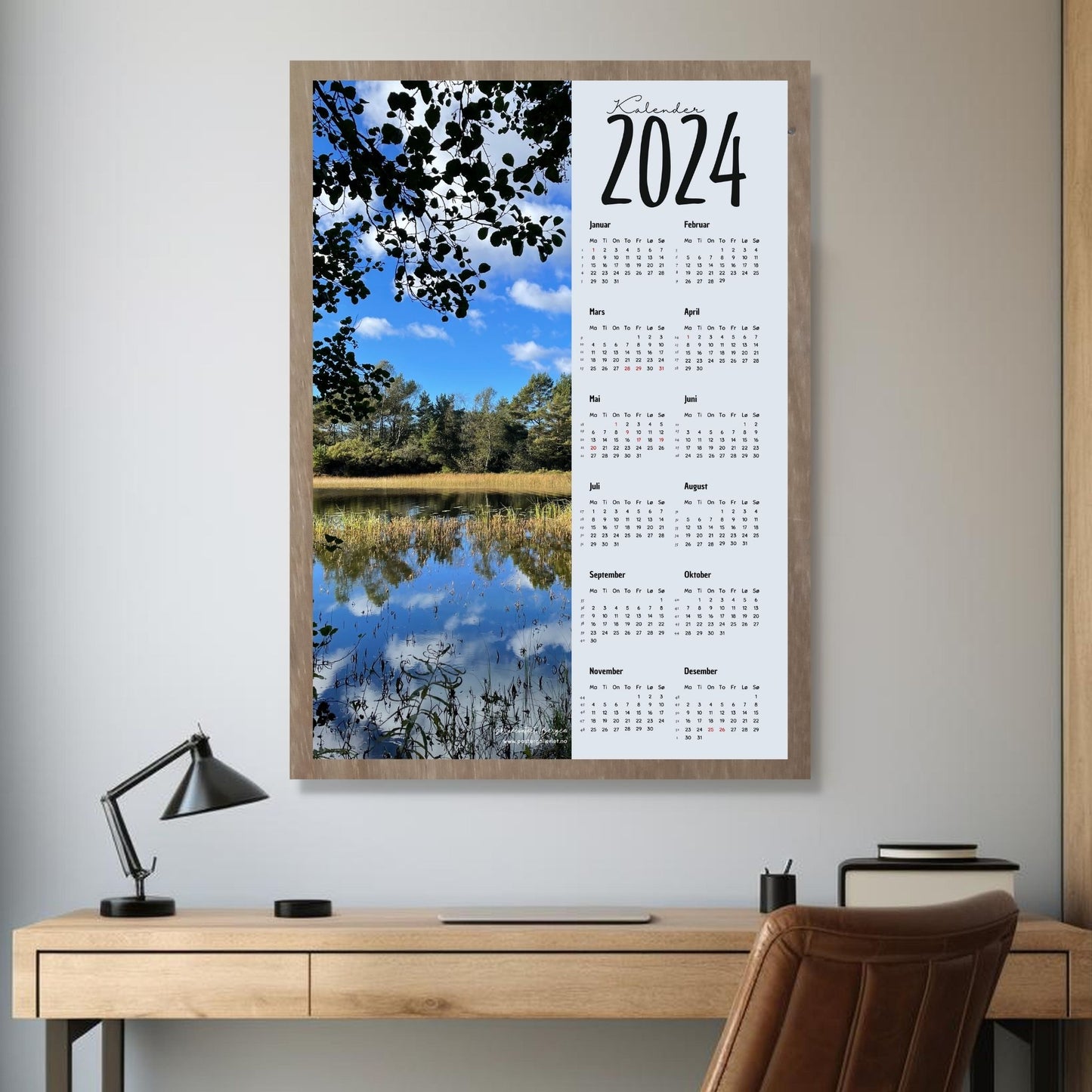 Kalender 2024 i grafisk print med fotomotiv. Halve vertikale side er et høstbilde fra Skranevatnet ved Sandsli, Bergen. Den andre halvdelen er påført 12 måneder med ukenummer og anmerket høytidsdager. Miljøbilde av kalender i eikeramme som henger på en vegg.