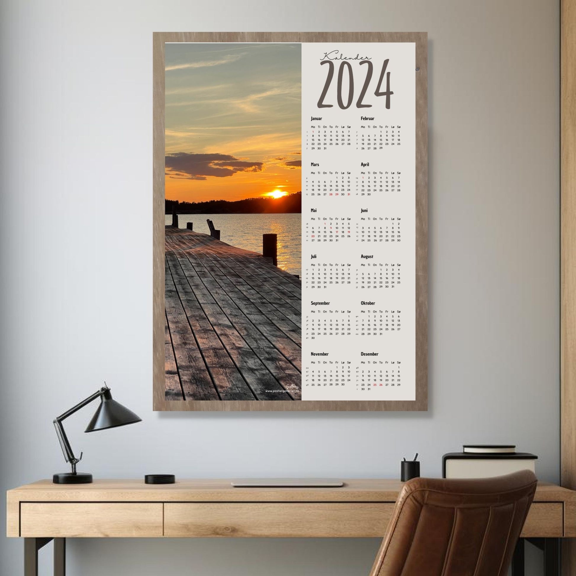 Kalender 2024 i grafisk print med fotomotiv. Halve vertikale side er et fotografi av en vakker solnedgang ved en brygge ved Saltnes, Råde. Den andre halvdelen er påført 12 måneder med ukenummer og anmerket høytidsdager. Miljøbilde av kalender i eikeramme som henger på en vegg.