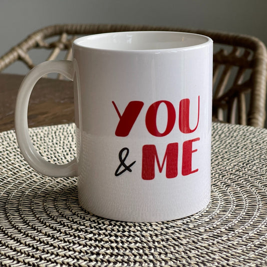 Krus i keramikk med teksten "YOU & ME" og en dristig typografi med et rødt fingeravtrykk-hjerte.