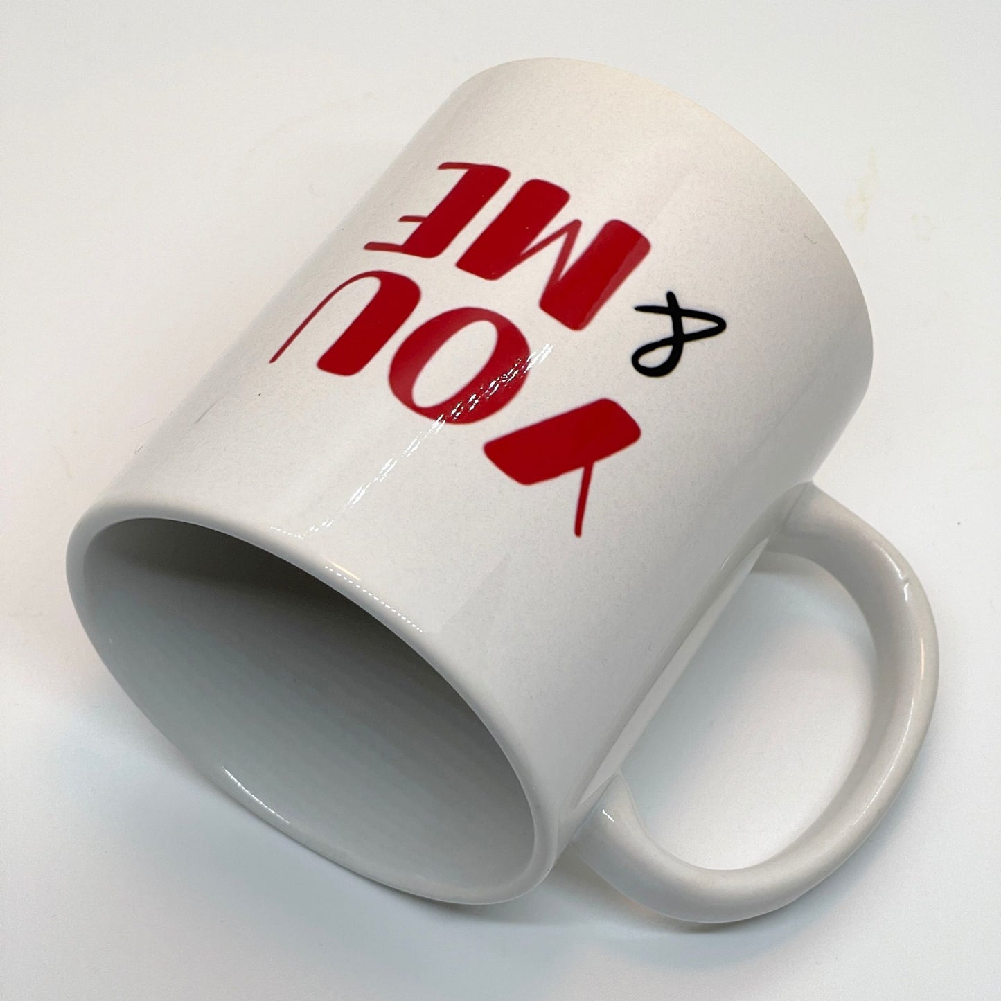 Krus i keramikk med teksten "YOU & ME" og en dristig typografi med et rødt fingeravtrykk-hjerte.