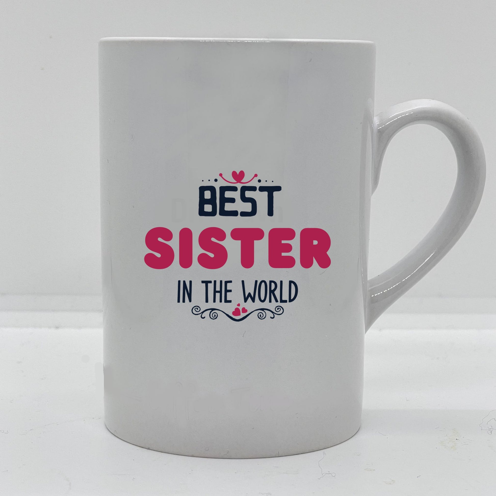 Krus i hvit keramikk med påskrift "Best sister in the world" på en side, og tre hjerter på motsatt side. Trykk i sort og rosa.