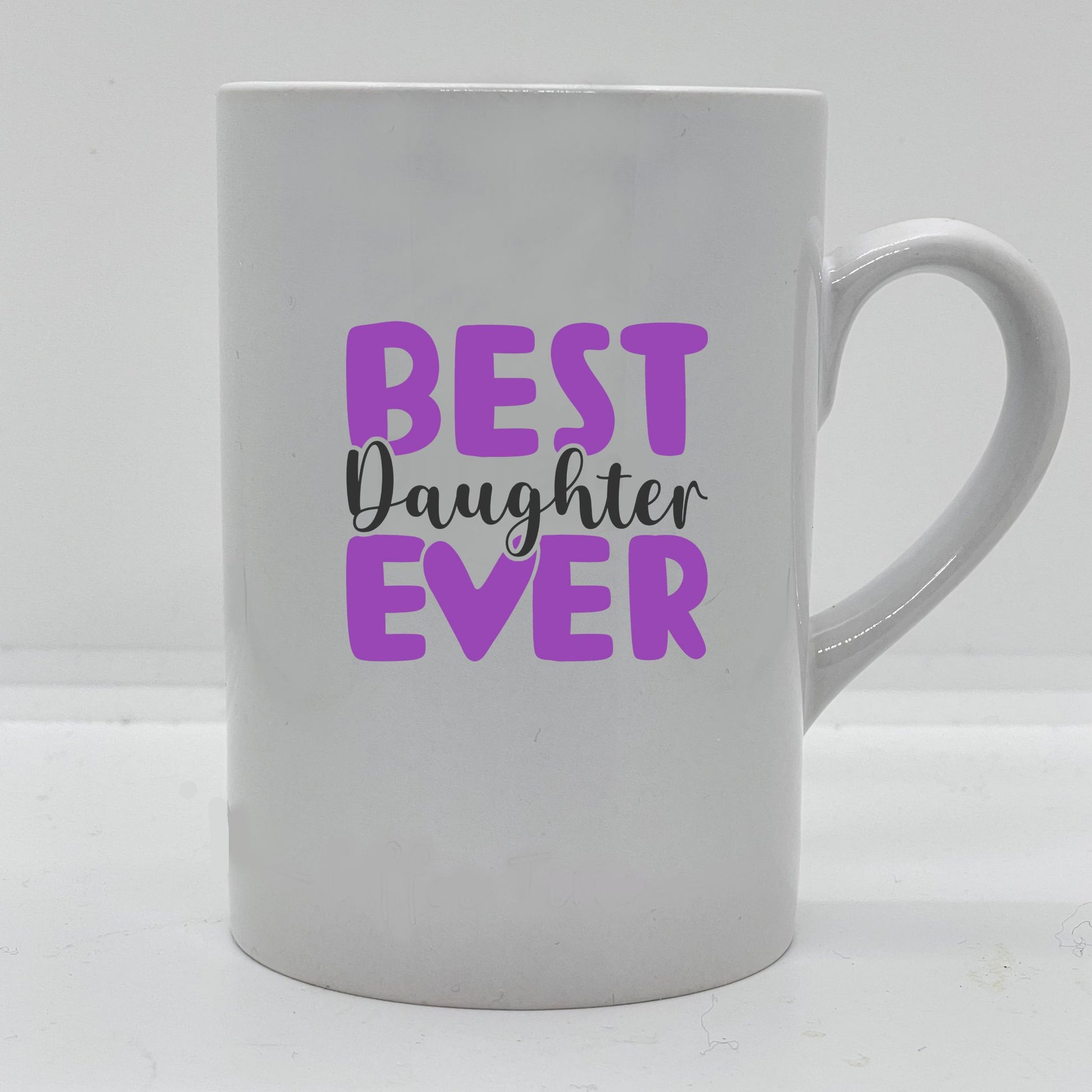 Krus i hvit keramikk med påskrift "Best daughter ever" på en side, og tre hjerter på motsatt side. Trykk o sort og lilla.
