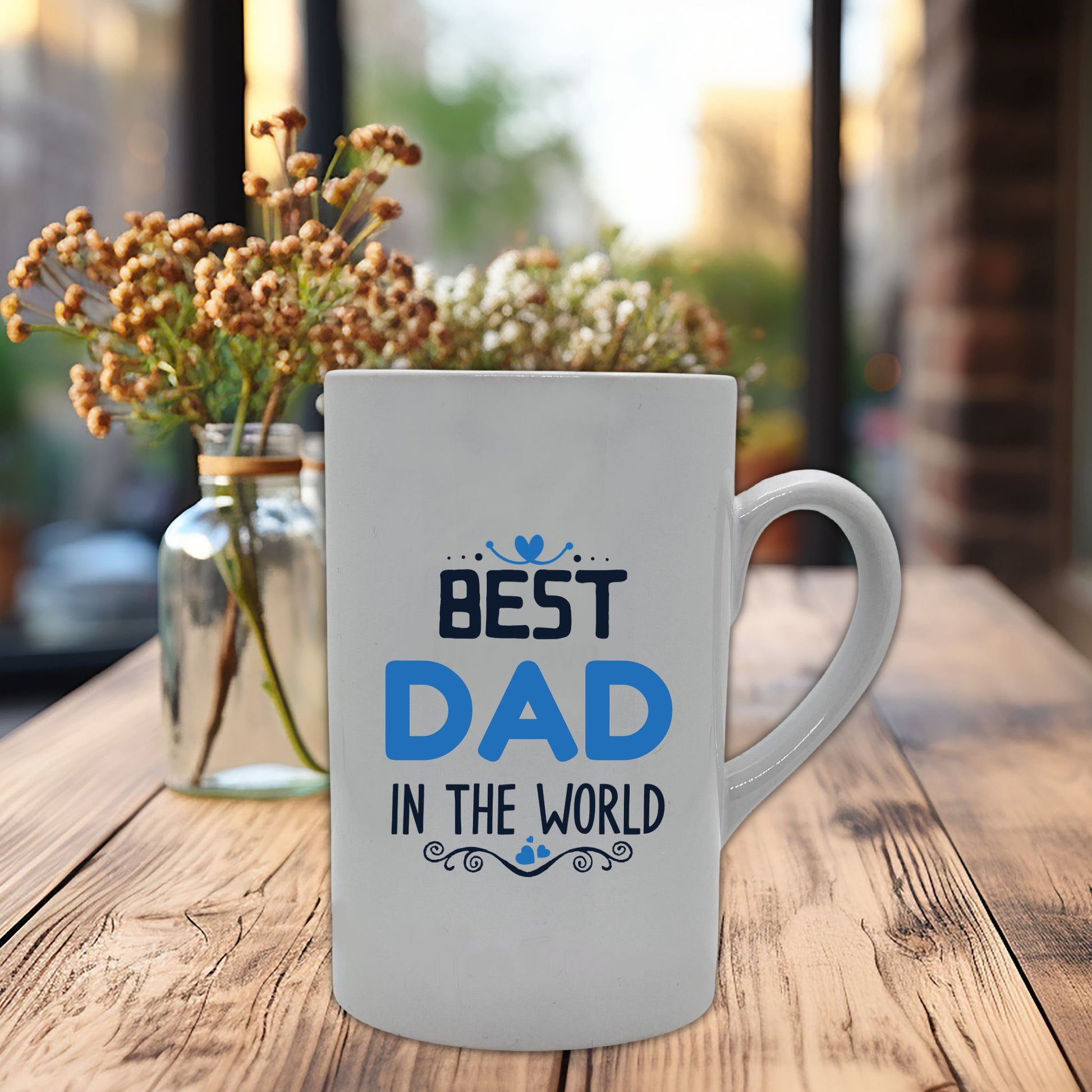 Krus i hvit keramikk med påskrift "Best dad in the world" på en side og tre hjerter på motsatt side. Trykk i lys blå og sort.