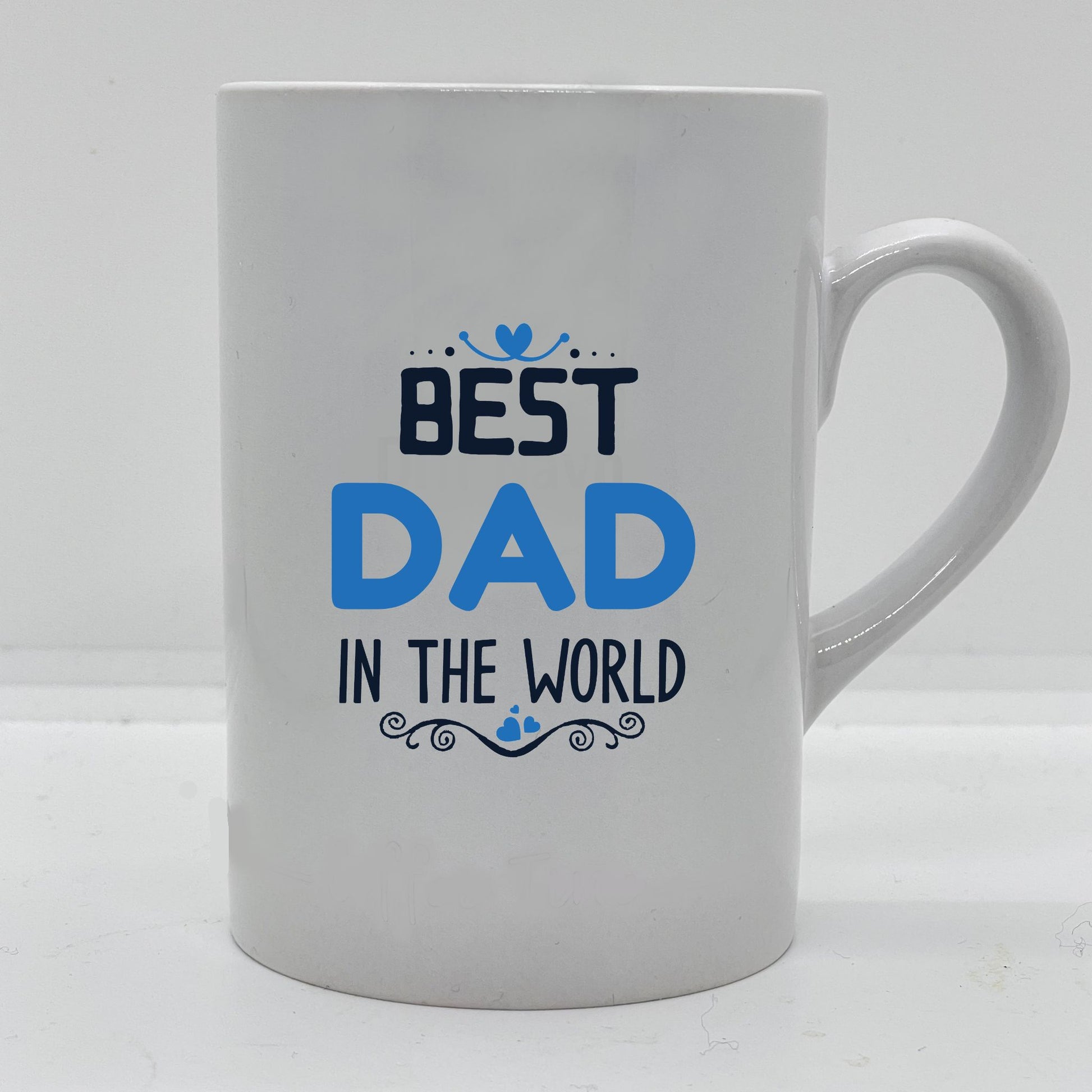 Krus i hvit keramikk med påskrift "Best dad in the world" på en side og tre hjerter på motsatt side. Trykk i lys blå og sort.