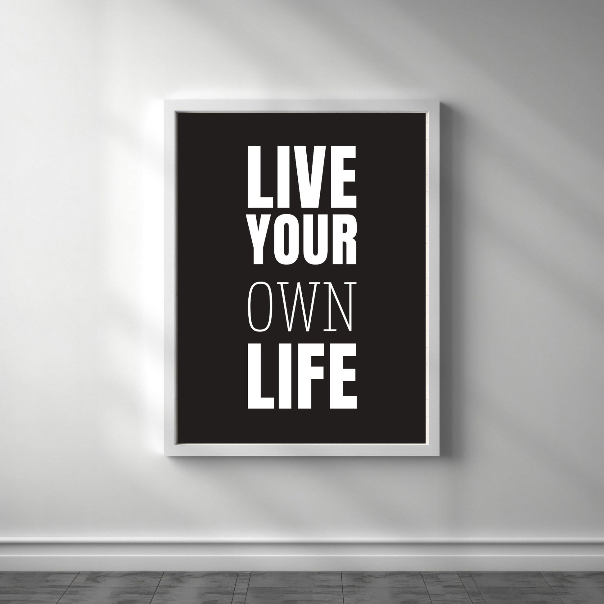 Grafisk plakat med hvit skrift på sort bakgrunn. Tekst på plakat "Live your own life" Illustrasjon viser plakat i hvit ramme.