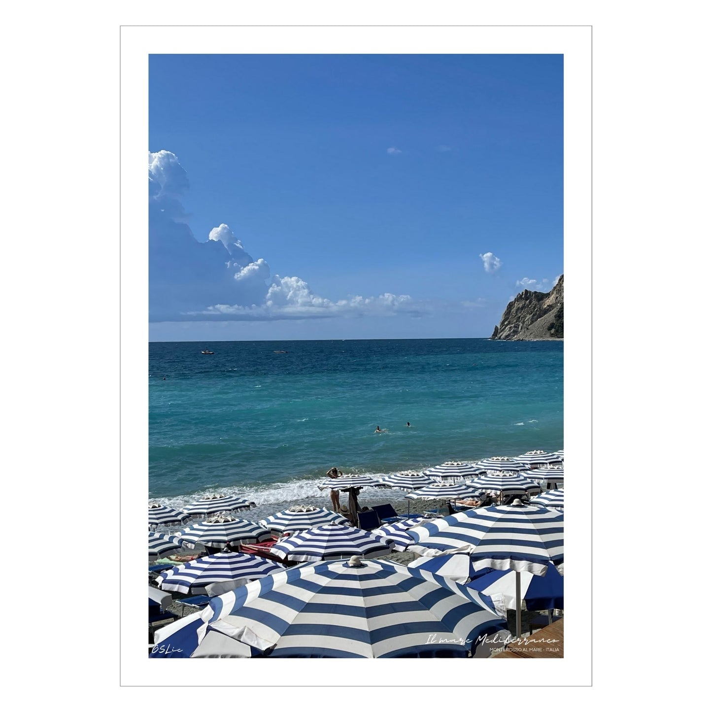 Motiv fra Montereosso al Mare, en av de fem byene i Cinque Terre ved Liguriakysten i Italia. Bildet viser blått middelhav og himmel som helt ned i vannet i horisonten. På høyre side skimtes noen klipper. På sranden er det tett i tett med blå og hvitstripete parasoller.