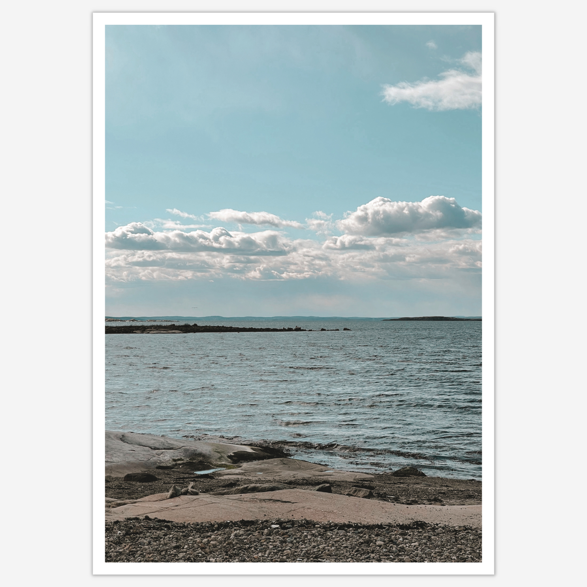 Himmel møter hav ved Saltholmen. Strand med svaberg, krusninger på sjøen og en blå himmel med hvite skyer.
