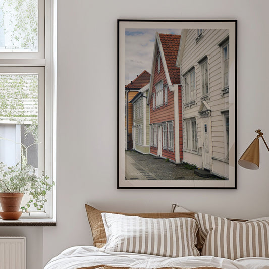 Nøstegaten på Nøstet er preget av tradisjonelle trehus tett i tett, med klare linjer og særpregede fasader. Illustrasjon viser plakat i sort ramme.
