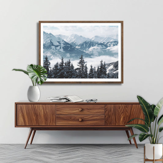 Dette vakre bildet viser et landskap dekket av snø og lett tåke, med dramatiske fjelltopper og trær som strekker seg opp mot himmelen. Illustrasjonsfoto viser motivet som plakat i brun ramme.