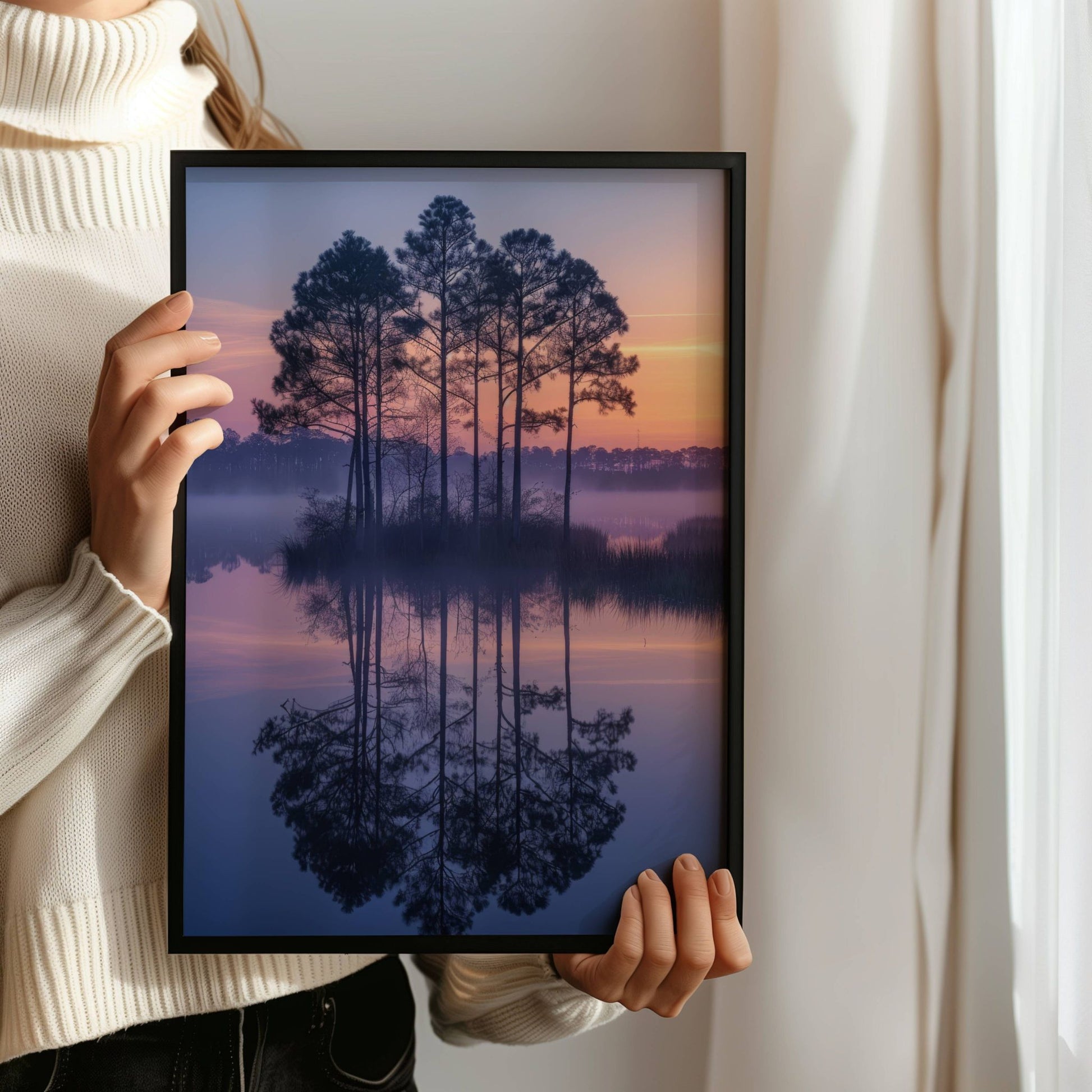 Dette harmoniske motivet fanger de tidlige morgentimene ved et stille vann, der furutrær speiler seg i det blikkstille vannet og himmelen gløder i varme pastelltoner. Illustrasjon viser motivet som plakat uten hvit kantlinje i sort ramme.