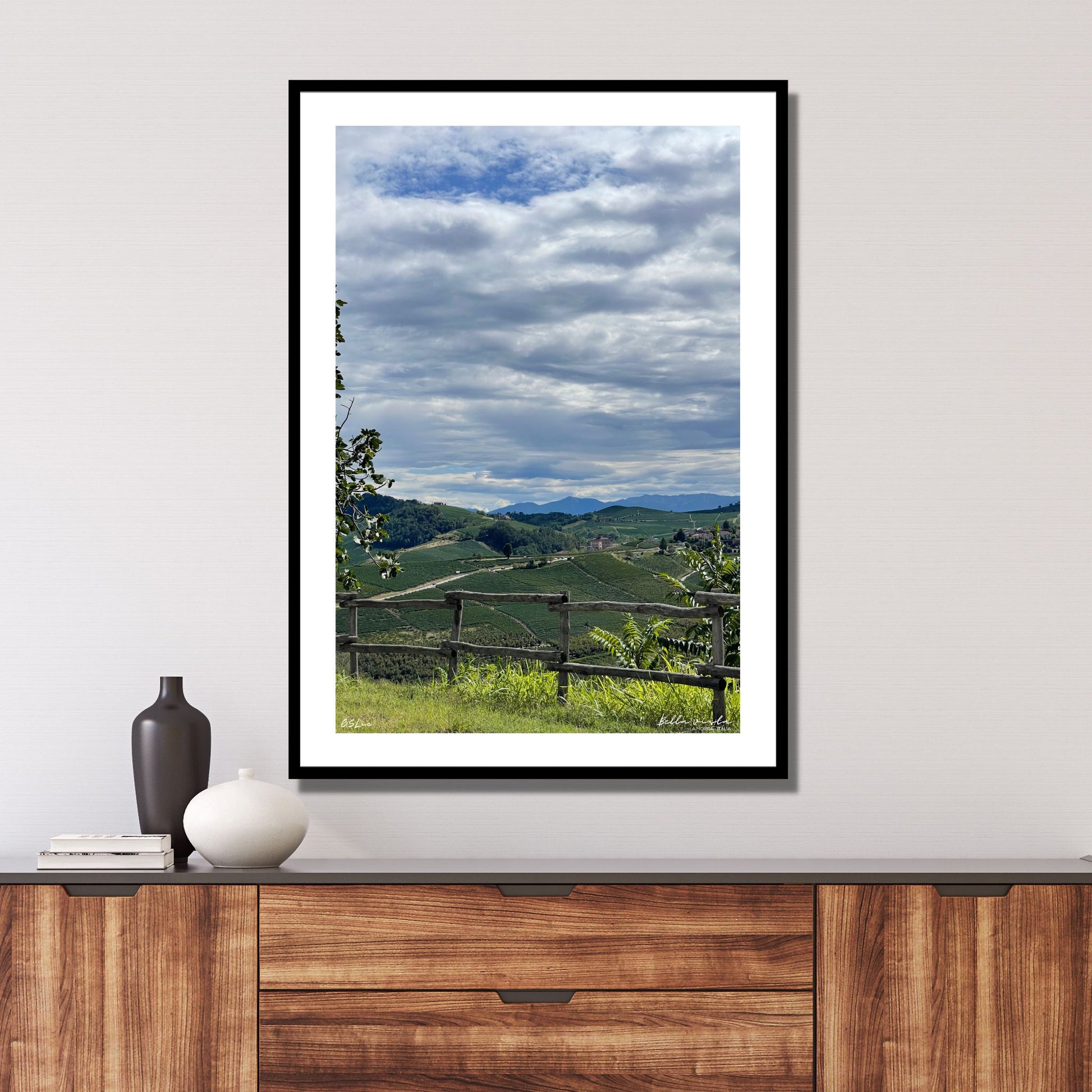 Utsikt mot Barolo fra vinmarker i La Morra området. Alpene kan skimtes i det fjerne. I forkant er det et tre gjerde. Det er et tett skylag på himmelen med en liten åpning hvor det skimtes blå himmel.
