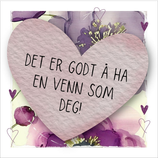 Go'ord plakat med et lilla hjerte med teksten "Det er godt å ha en venn som deg" på en bakgrunn med blomstermotiv i lilla, burgunder og grønt. Hvit kant på 1,5 cm. som fremhever og gir bildet dybde.