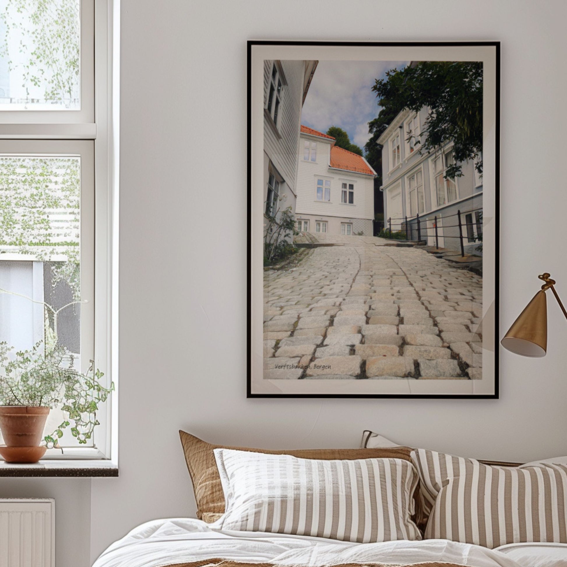 Verftsbakken leder ned mot sjøen og er preget av brostein og hvitmalte trehus – et typisk Nordnes-miljø med historisk sus. Illustrasjon viser plakat i sort ramme.