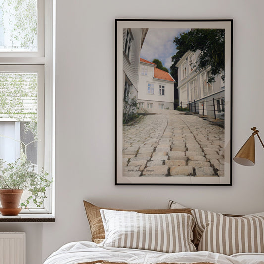 Verftsbakken leder ned mot sjøen og er preget av brostein og hvitmalte trehus – et typisk Nordnes-miljø med historisk sus. Illustrasjon viser plakat i sort ramme.