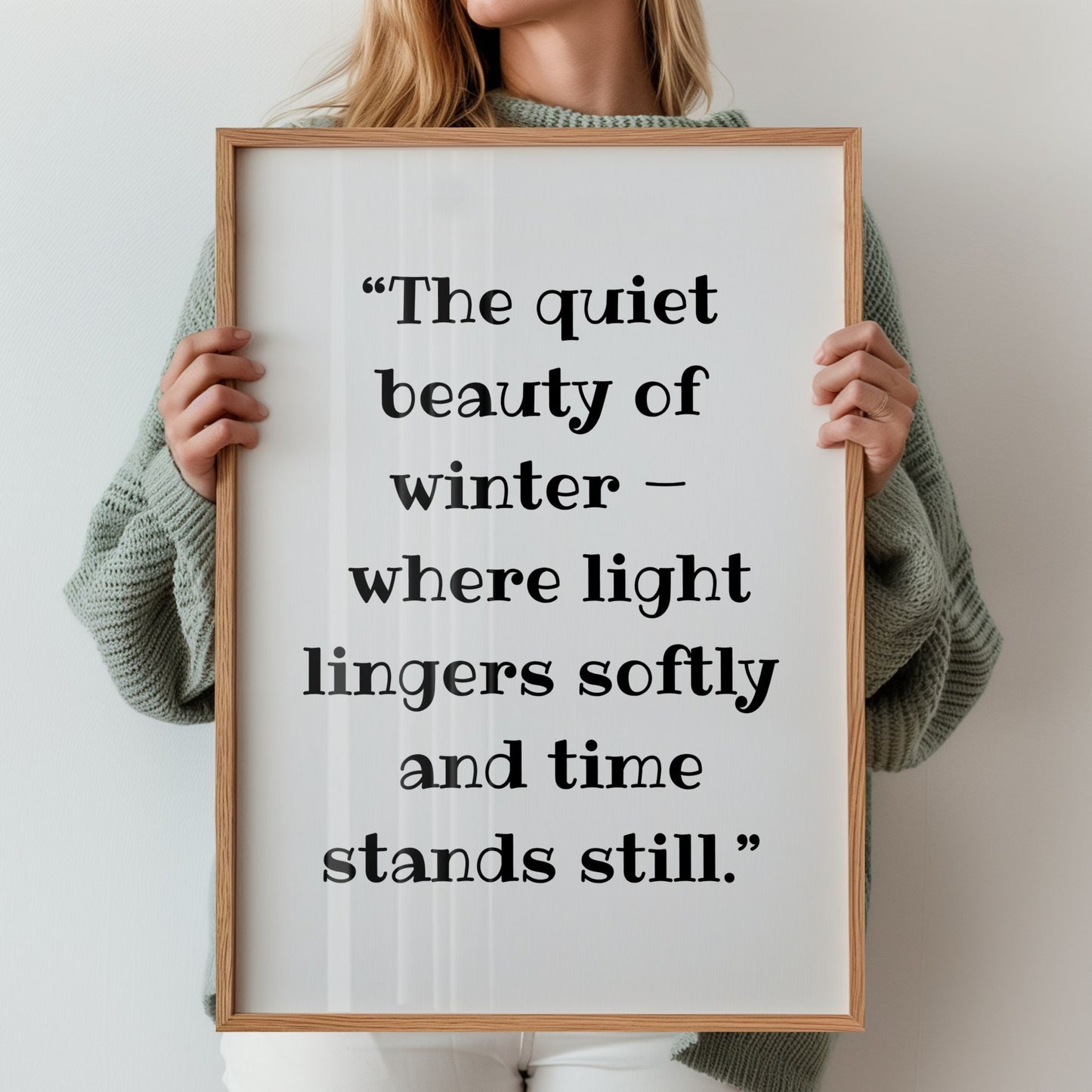 Kvinne holder rammet vinterplakat med teksten ‘The quiet beauty of winter – where light lingers softly and time stands still.’
