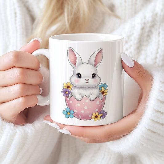 Keramikkrus med søt hvit kanin som sitter i rosa påskeegg med blomster, holdt i hendene foran lys bakgrunn.