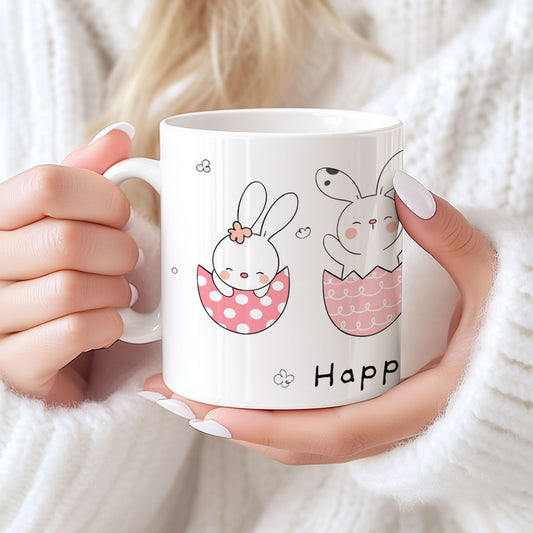 Keramikkrus med søte kaniner som sitter i rosa eggeskall, holdt i hendene foran lys bakgrunn.