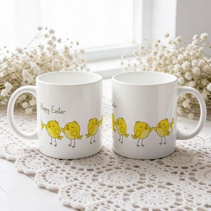 Påskekrus med gule kyllinger på rekke og teksten Happy Easter, vist fra begge sider på hvit blondeduk.