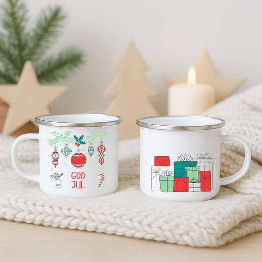 Hvitt emaljekrus med to grafiske julemotiver: hengende ornamenter med teksten «God Jul» og en minimalistiske julegaver i rødt og grønt, fotografert på lys strikket duk med juledekor i bakgrunnen.