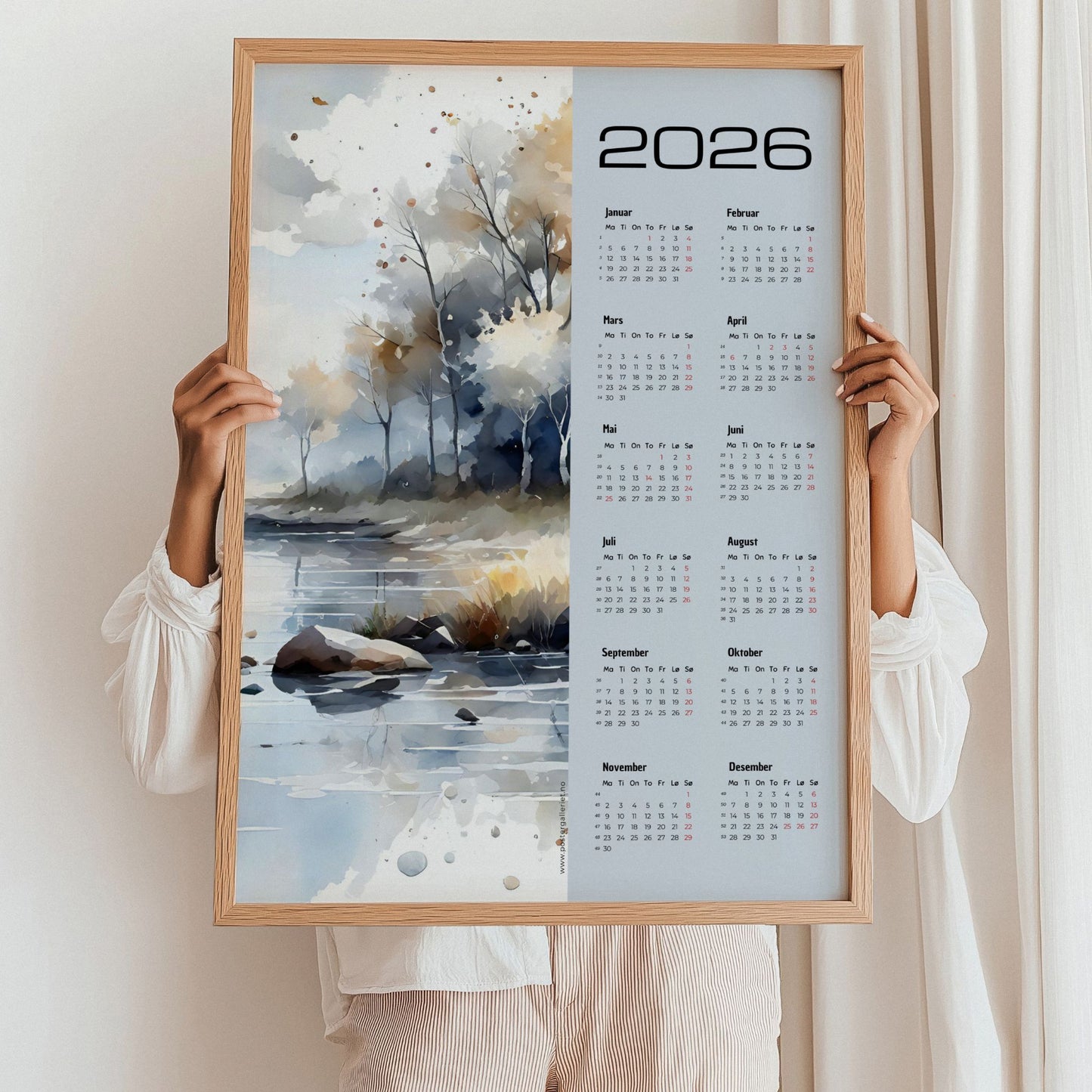 Kalender 2026 med akvarellmotiv av høstlig landskap ved vann, i lyse og varme toner. Illustrasjon viser kalender i eik ramme.