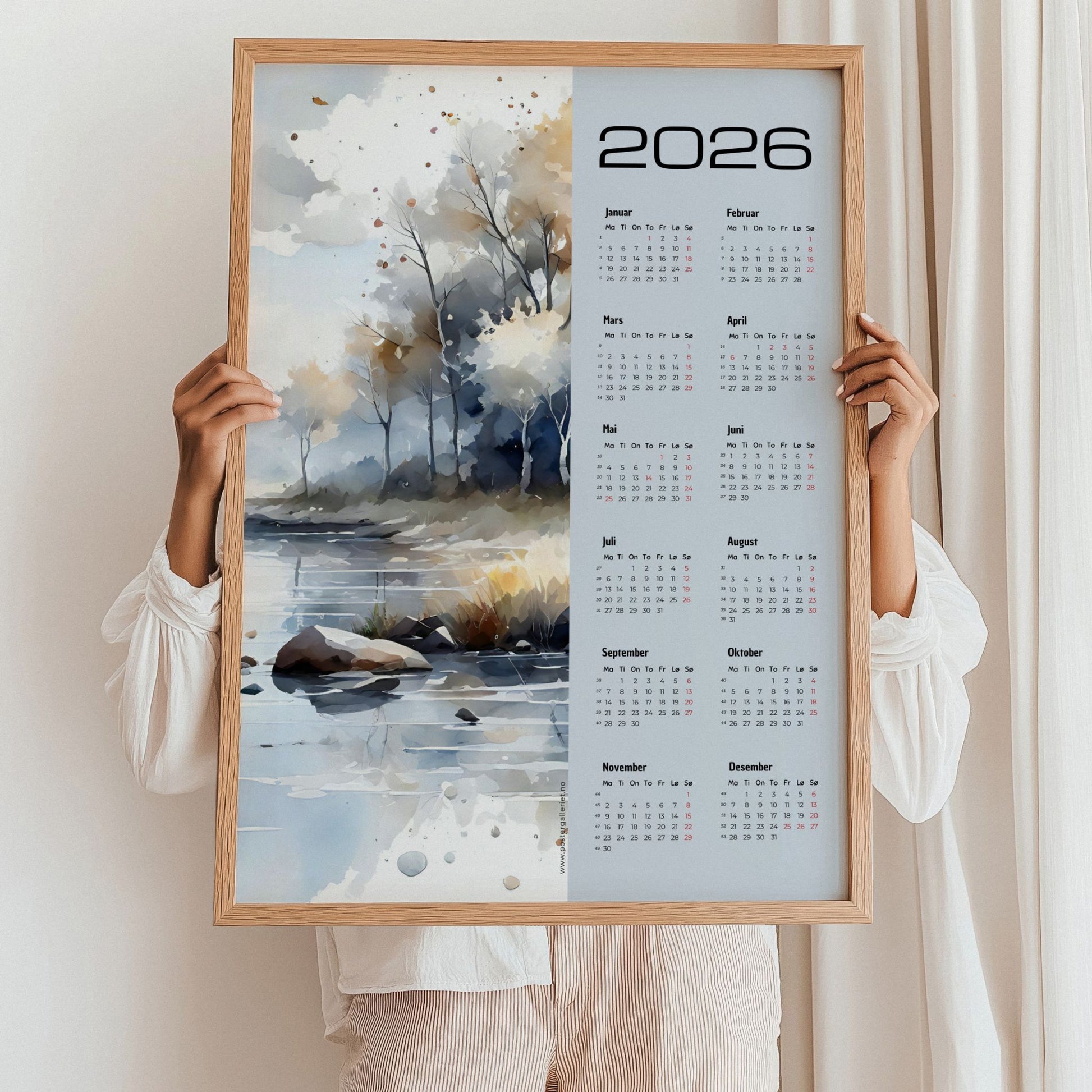 Kalender 2026 med akvarellmotiv av høstlig landskap ved vann, i lyse og varme toner. Illustrasjon viser kalender i eik ramme.