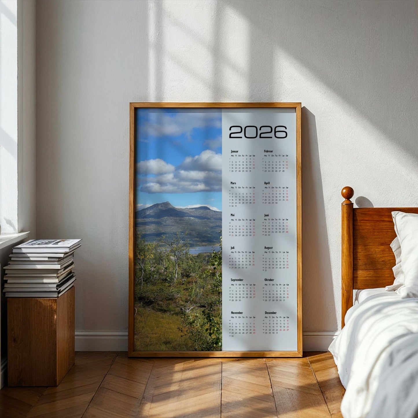 Kalender 2026 med foto av Dærgafjellet i Røyrvik, sett over fjellterreng og høstlig vegetasjon. Illustrasjon viser kalender i eik ramme på et soverom.