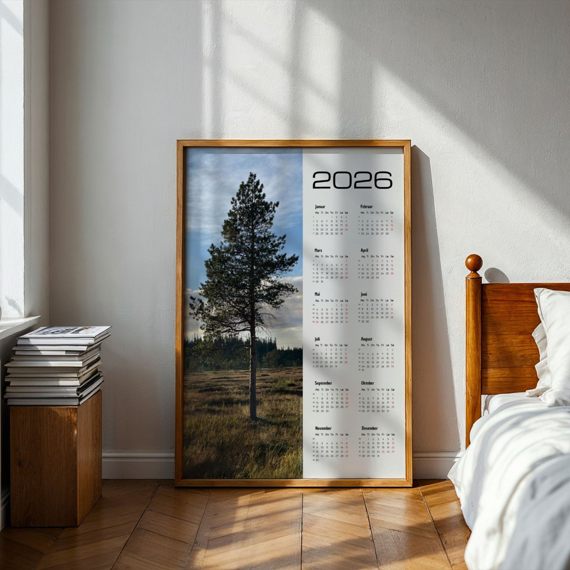 Kalender 2026 med foto av en stor furu i kveldslys. Illustrasjon viser kalender i eik ramme på et soverom.
