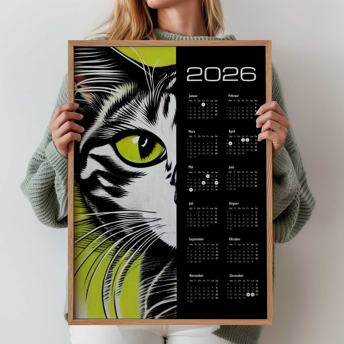 Kalender 2026 med grafisk illustrasjon av katt i svart, hvitt og grønt. Illustrasjon viser kalender i eik ramme.