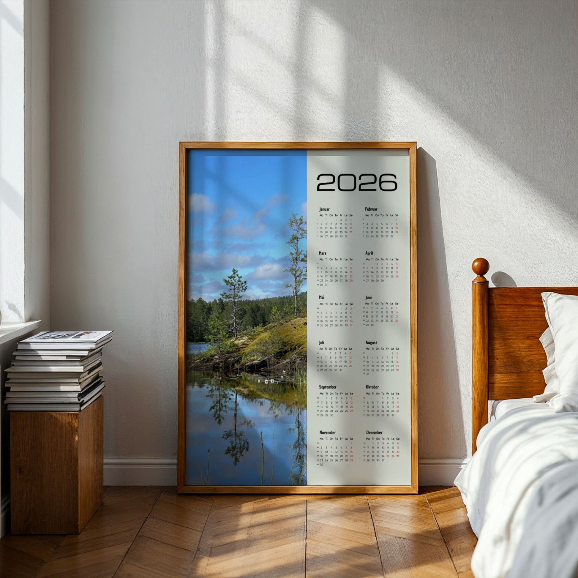 Fotokalender 2026 med landskapsmotiv fra Midterfjellet i Steinkjer, stille vann som speiler skog og himmel, med norsk kalender og røde dager. Illustrasjon viser kalender i eik ramme på et soverom.