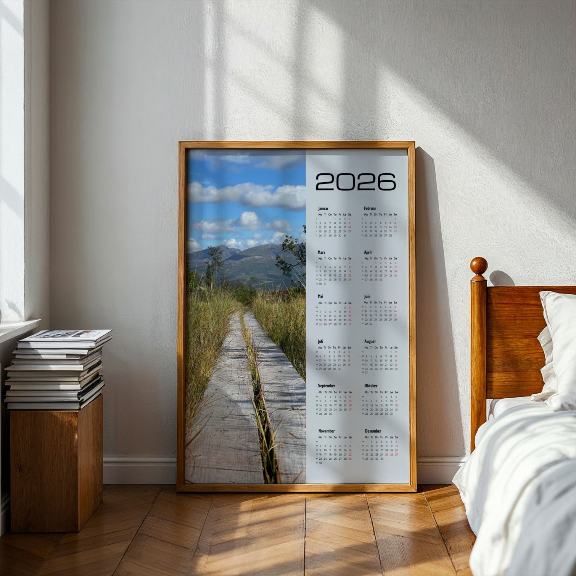 Kalender 2026 med foto av en plankesti som leder inn i fjellandskapet. Illustrasjon viser kalender i eik ramme på et soverom.