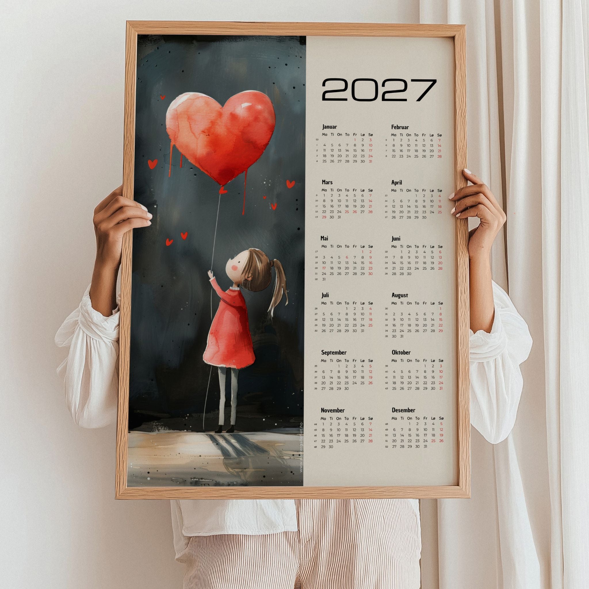 Kalender 2027 med illustrasjon av jente og rød hjerteballong, holdt opp i treramme