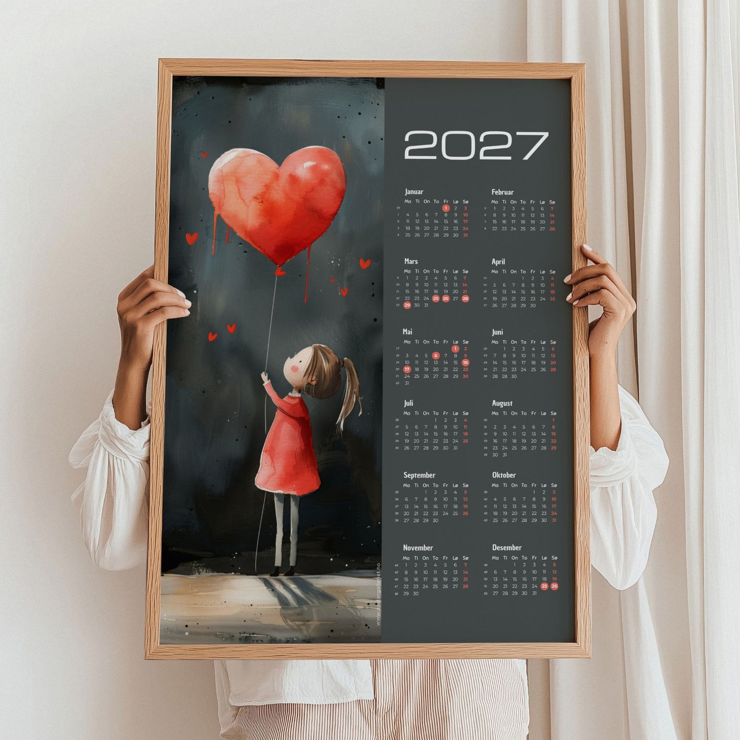 Kalender 2027 med pike, rød hjerteballong og mørk bakgrunn, holdt i eikeramme.