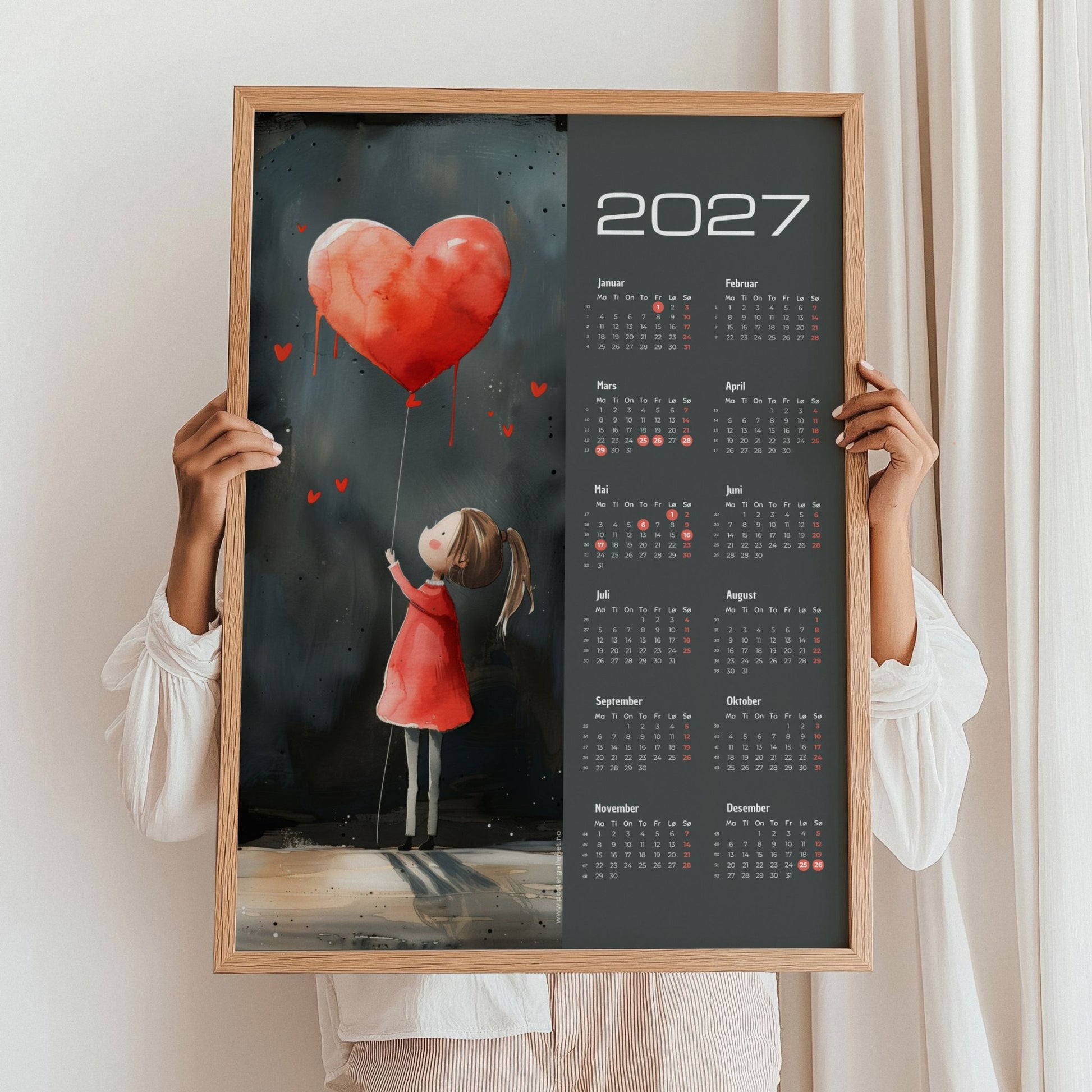 Kalender 2027 med pike, rød hjerteballong og mørk bakgrunn, holdt i eikeramme.