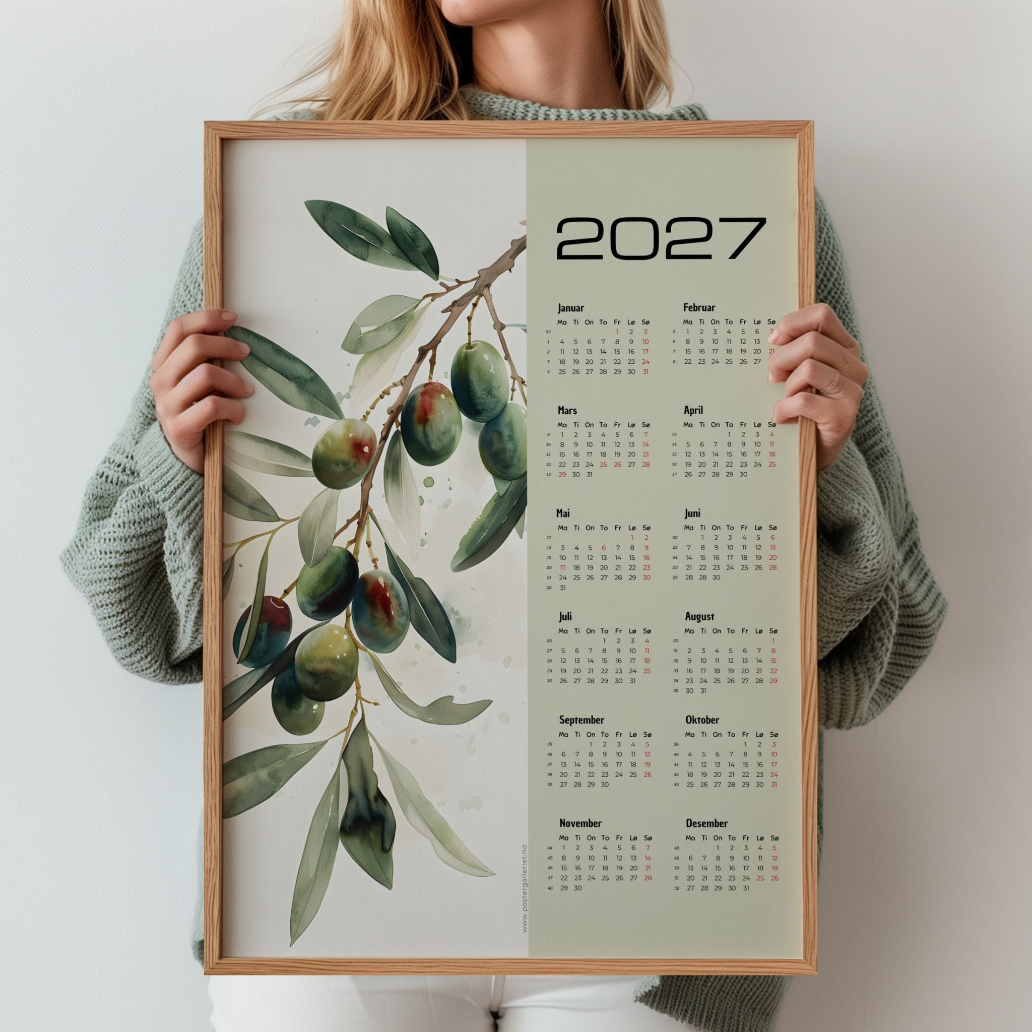 Illustrert kalender 2027 med olivengren i grønne naturtoner, holdt opp i eikeramme