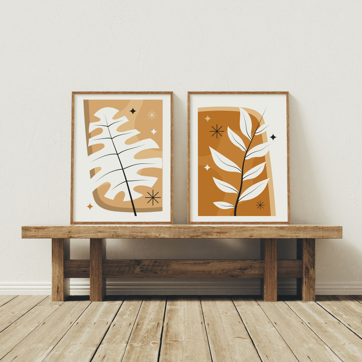 Monstera Glow og Golden Branch grafiske boho-plakater i trerammer plassert sammen på rustikk trebenk