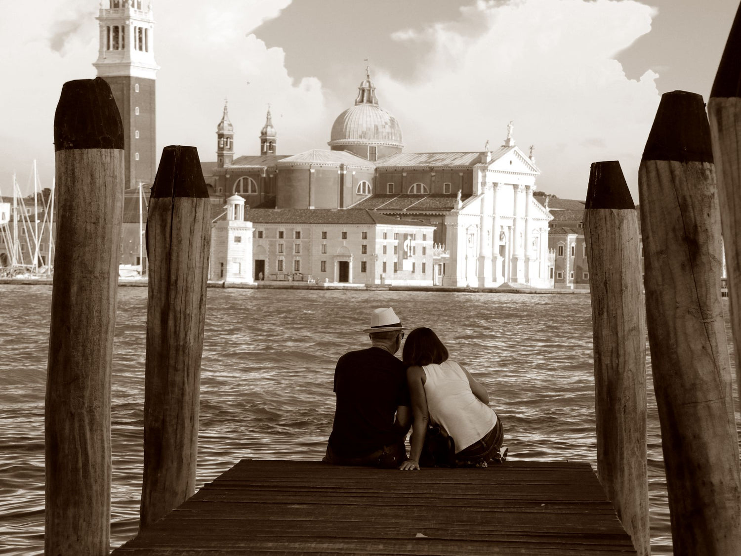 Par som sitter sammen på en brygge i Venezia i solnedgang – stemningsfullt fotografi av kjærlighet og nærhet