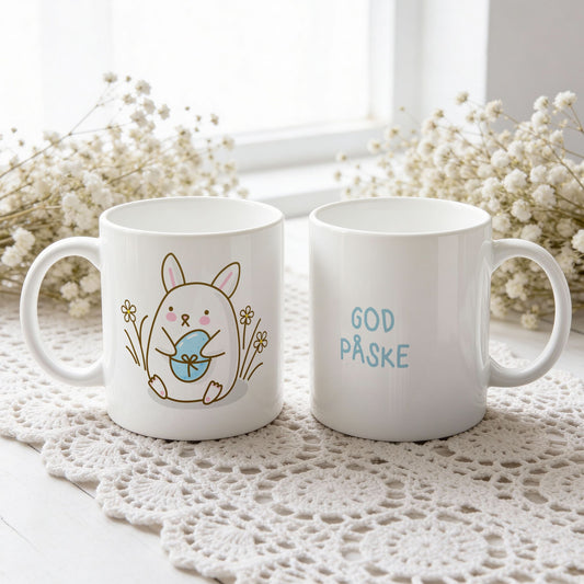 Hvitt keramikkrus med søt påskehare som holder lyseblått påskeegg og teksten God påske i blå tone på motsatt side.